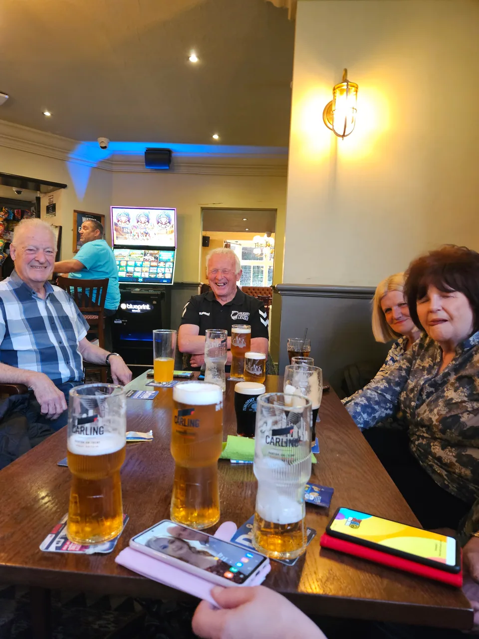 A group of quiz teammates with drinks and phones around a pub table