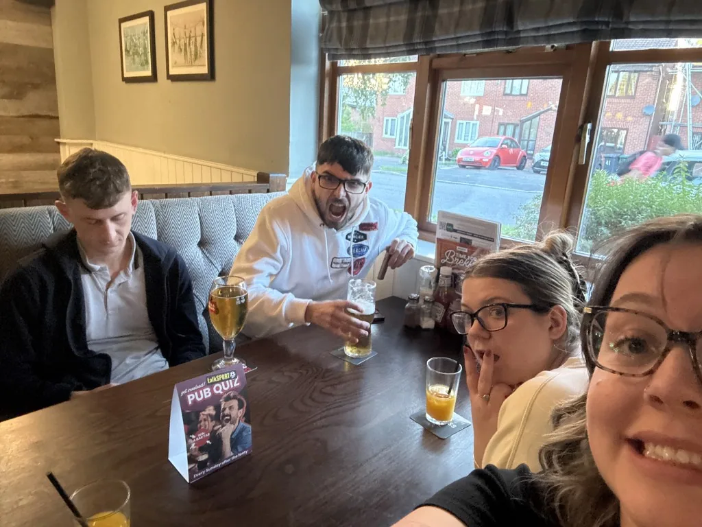 Four quiz teammates at a pub table, with phones ready to play